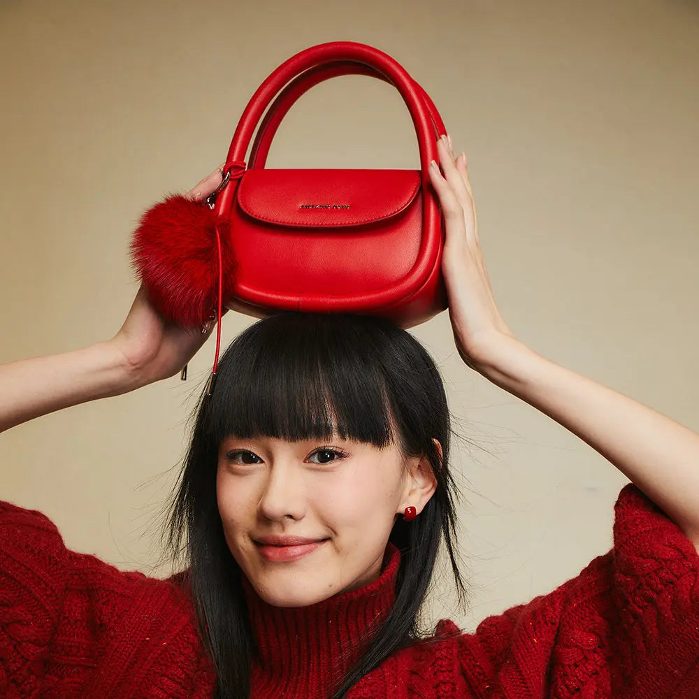 Smiling woman in red sweater holding red handbag with pompom on head, Amazing Song brand