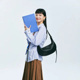 Smiling woman with blue book, striped shirt, brown skirt, and black shoulder bag
