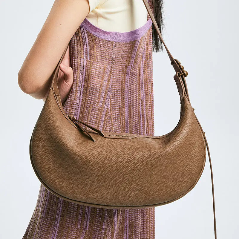 Woman wearing a textured brown shoulder bag with adjustable strap and stylish knit dress