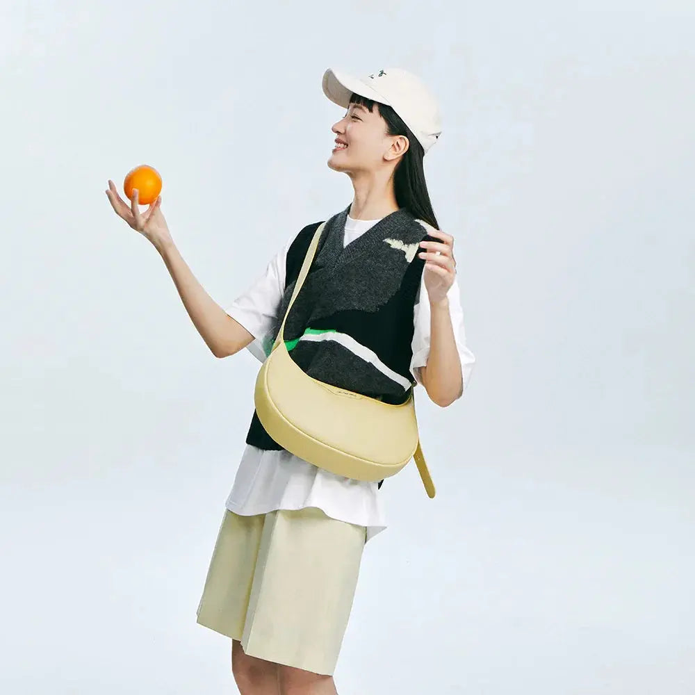 Smiling woman in a casual outfit with a light yellow sling bag holding an orange, Amazing Song official website