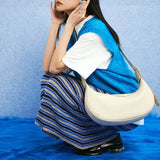 Woman in blue knit vest and striped skirt posing with cream shoulder bag on blue furry rug, Amazing Song