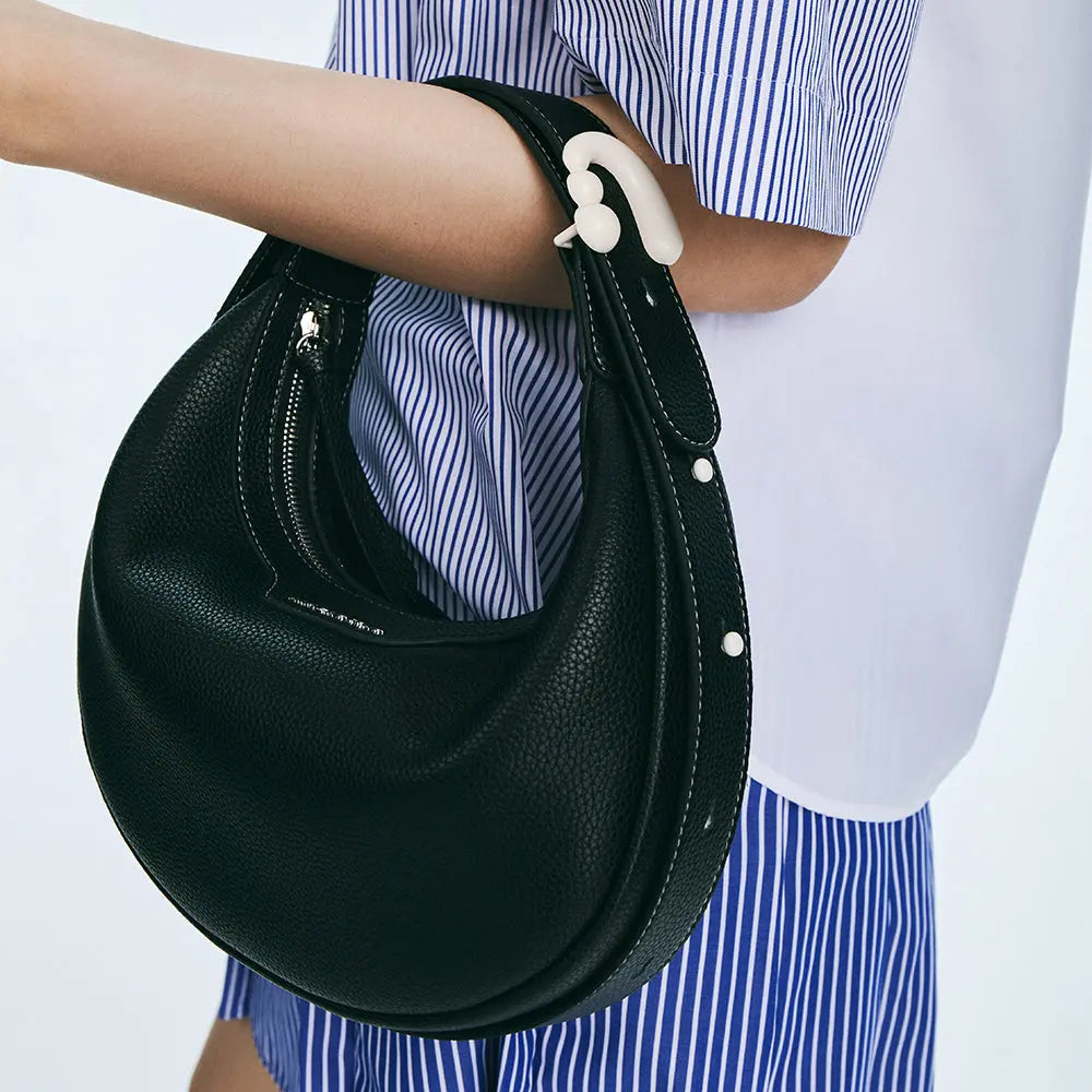 Black leather shoulder bag with white accents, worn with a blue striped shirt, Amazing Song