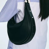 Black leather shoulder bag with white stitching worn over striped shirt, Amazing Song