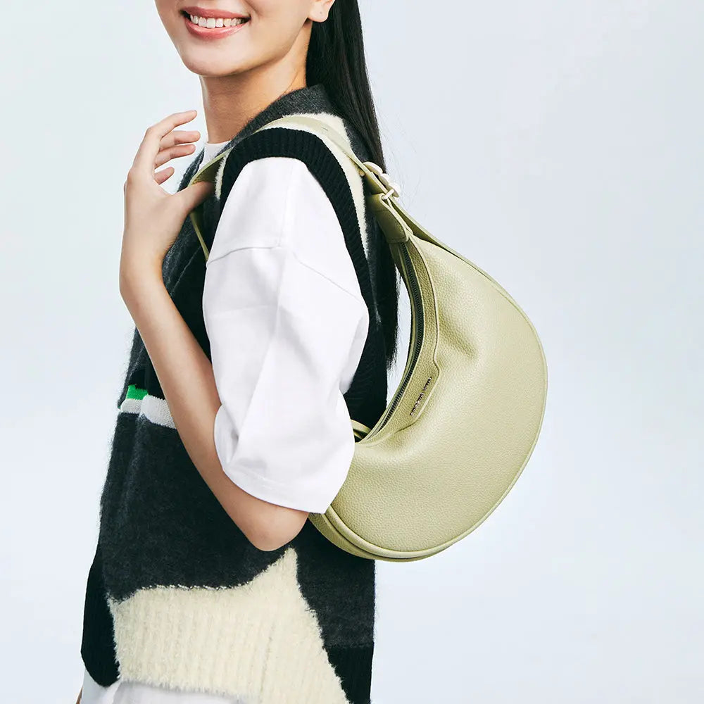 Smiling woman wearing a sleeveless sweater and white top, holding a light green shoulder bag