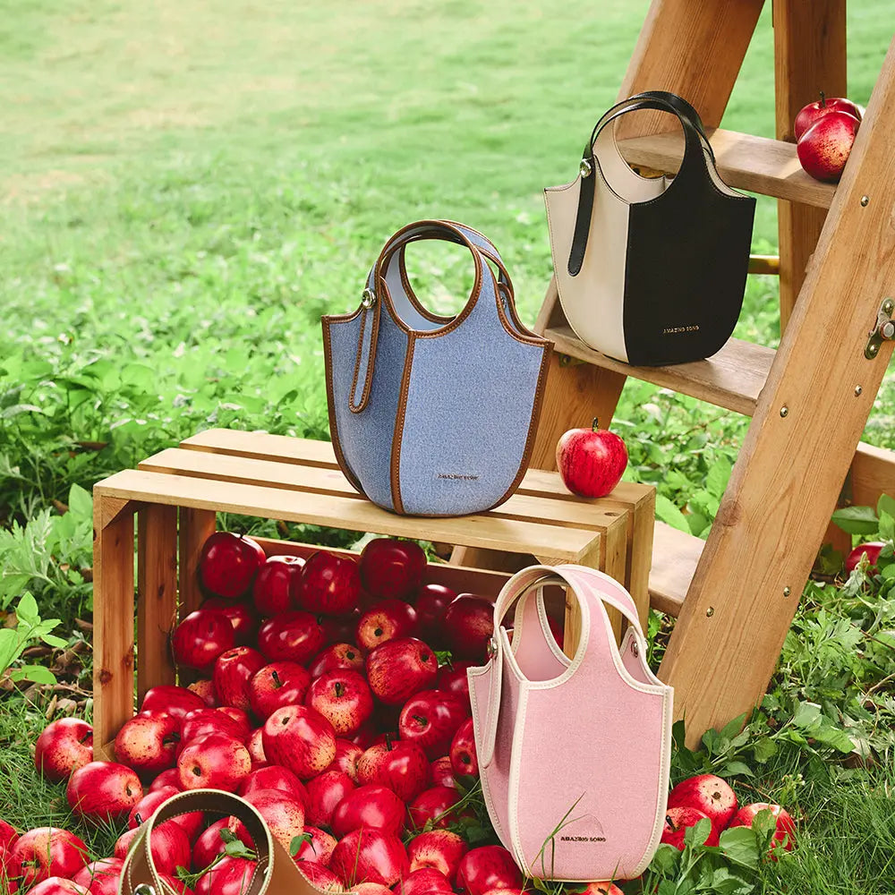 Amazing Song designer handbags in blue, black, and pink displayed outdoors with apples