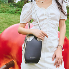 Woman in white dress with Amazing Song black crossbody bag outdoors, large apple sculpture in background