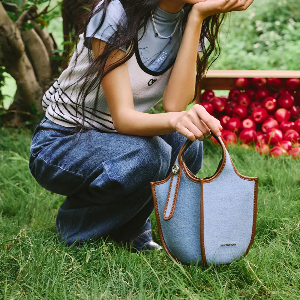 Woman outdoors with denim Amazing Song bag on grass, apples in background