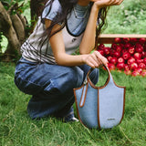 Woman outdoors with denim Amazing Song bag on grass, apples in background
