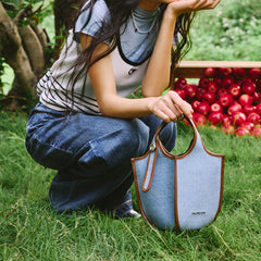 Woman outdoors with denim Amazing Song bag on grass, apples in background