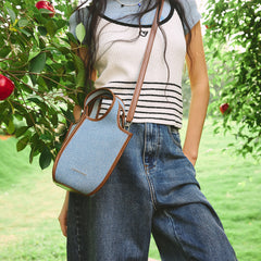 Woman in striped top and jeans with blue Amazing Song crossbody bag outdoors near apple tree