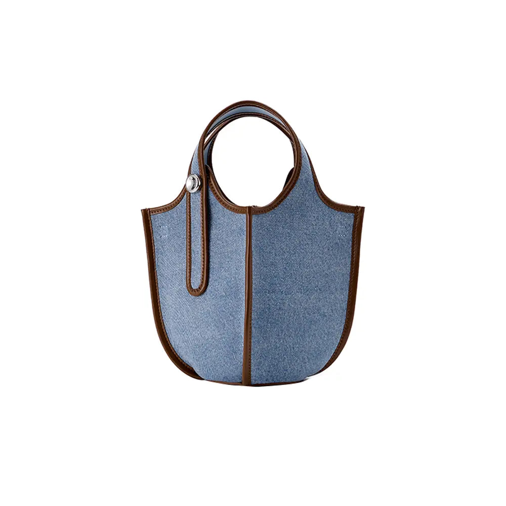 Blue denim tote bag with brown leather trim and round handles on white background