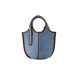 Blue denim tote bag with brown leather trim and round handles on white background