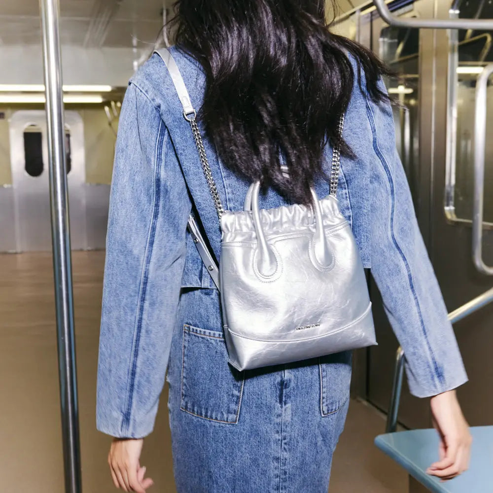 Woman in denim jacket with metallic silver Amazing Song bag on subway train