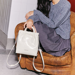 Woman with grey sweater and skirt holding white Amazing Song handbag on brown chair