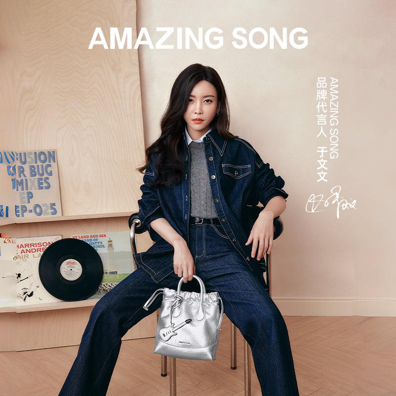 Woman in denim outfit holding silver Amazing Song handbag, vinyl records in background, official brand promo.