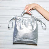 Hand holding metallic silver Amazing Song handbag against white textured background