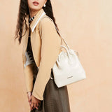 Woman modeling beige jacket and plaid skirt with white Amazing Song handbag