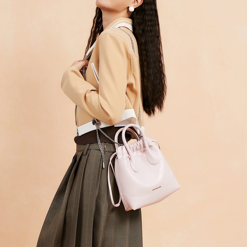 Woman wearing a tan jacket carrying a pastel pink Amazing Song bucket bag