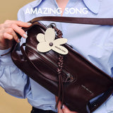 Amazing Song brown leather handbag with butterfly tag, held by person in blue shirt