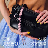 Amazing Song black leather handbag with pink braided flower accessory, held by woman in striped skirt