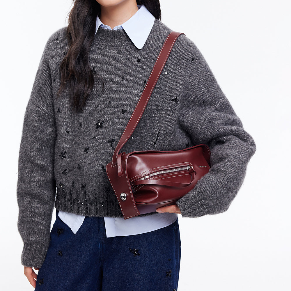 Woman wearing grey knit sweater and blue collared shirt holding burgundy leather shoulder bag