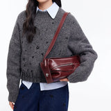 Woman wearing grey knit sweater and blue collared shirt holding burgundy leather shoulder bag