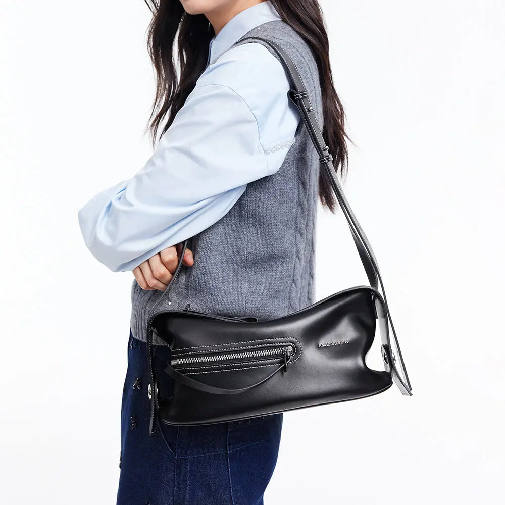 Woman carrying a black Amazing Song shoulder bag with zipper, styled with grey vest and blue shirt