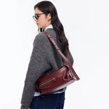 Woman in glasses and gray sweater wearing a burgundy Amazing Song shoulder bag