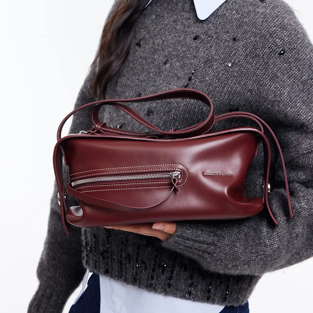 Amazing Song burgundy leather shoulder bag with zipper detail, held by model in grey sweater