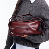 Amazing Song burgundy leather shoulder bag with zipper detail, held by model in grey sweater