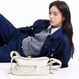 Woman in blue denim jacket and grey sweater with cream Amazing Song handbag