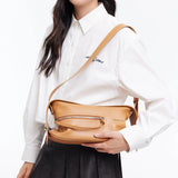 Woman in white shirt holding tan Amazing Song crossbody bag against white background