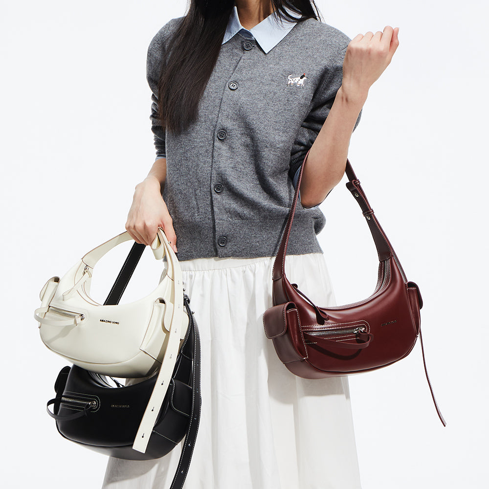 Woman holding white, black, and burgundy Amazing Song handbags, gray sweater, white skirt