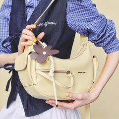 Woman holding Amazing Song cream shoulder bag with flower charm and braided detail
