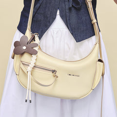Amazing Song cream shoulder bag with zipper pocket and flower charm, worn crossbody.