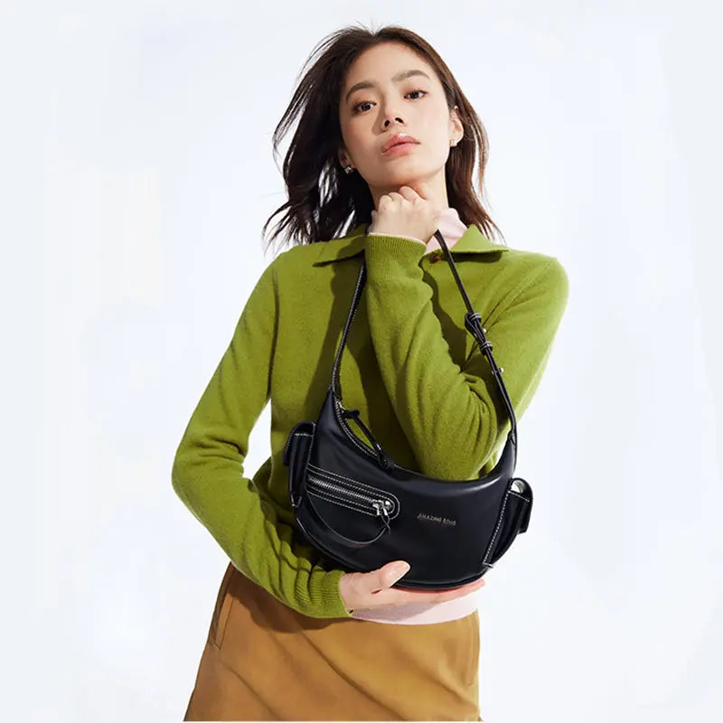 Woman in green sweater and brown skirt holding black Amazing Song shoulder bag