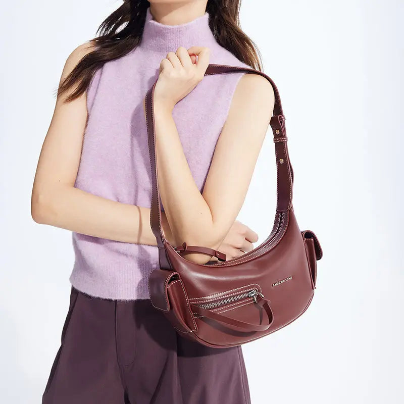 Woman modeling a burgundy Amazing Song shoulder bag with zipper pocket, wearing a sleeveless lavender top and dark pants.