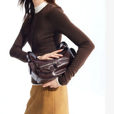 Woman in brown top and tan skirt holding a dark brown leather shoulder bag, Amazing Song