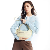 Woman in light blue cardigan holding cream Amazing Song handbag against white background