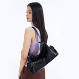 Woman in sleeveless lavender top carrying a sleek black Amazing Song shoulder bag