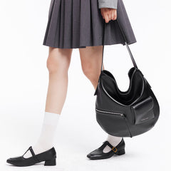 Woman in pleated gray skirt and black Mary Jane shoes holding a large black handbag