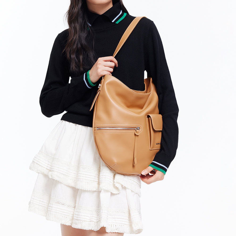 Woman wearing black sweater and white skirt holding tan leather shoulder bag