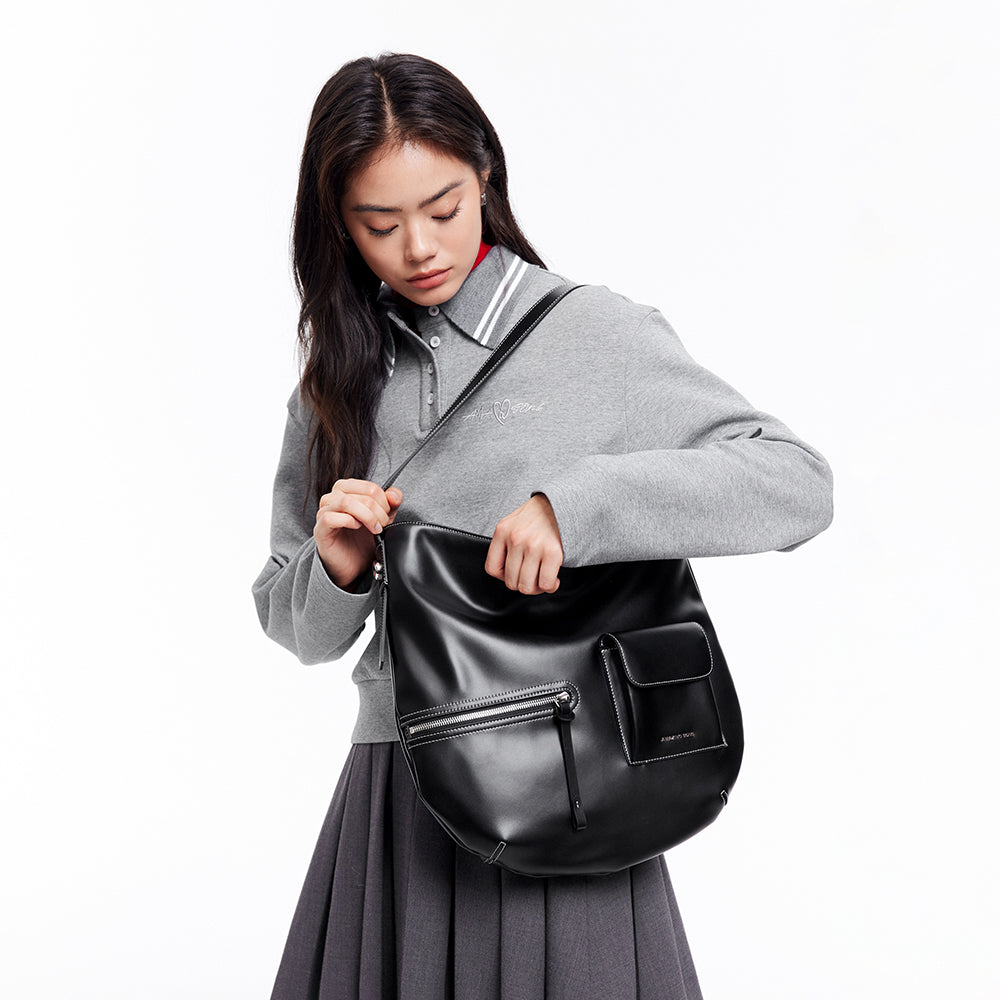 Woman in gray top and skirt holding a black Amazing Song shoulder bag against white background