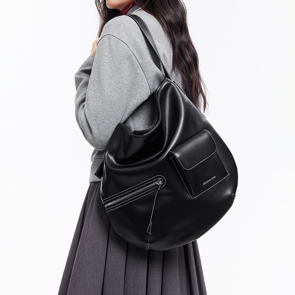 Woman in grey top with pleated skirt carrying large black Amazing Song shoulder bag