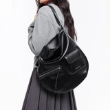 Woman in grey top with pleated skirt carrying large black Amazing Song shoulder bag