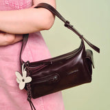 Brown leather Amazing Song shoulder bag with floral charm, held by person in pink dress