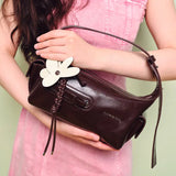 Woman in pink dress holding Amazing Song brown leather shoulder bag with white flower charm