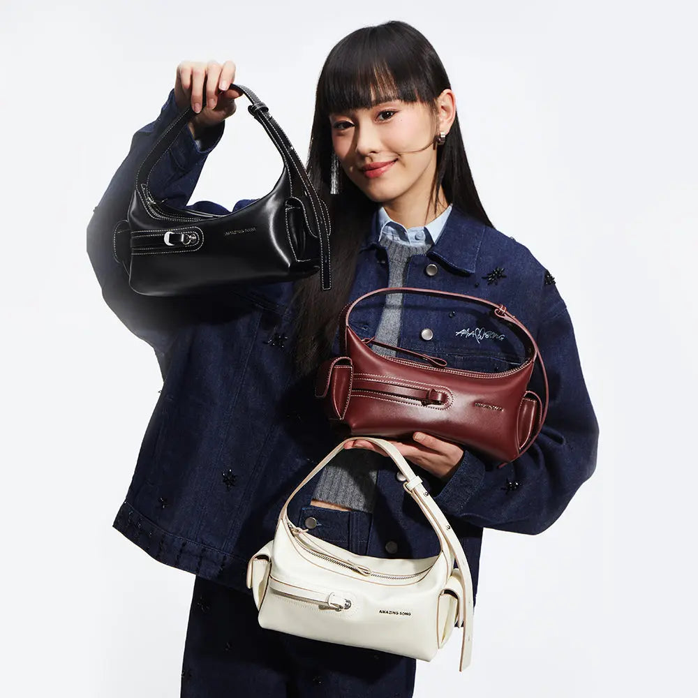 Woman in denim jacket holding three Amazing Song handbags in black, burgundy, and white