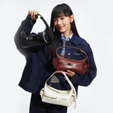 Woman in denim jacket holding three Amazing Song handbags in black, burgundy, and white