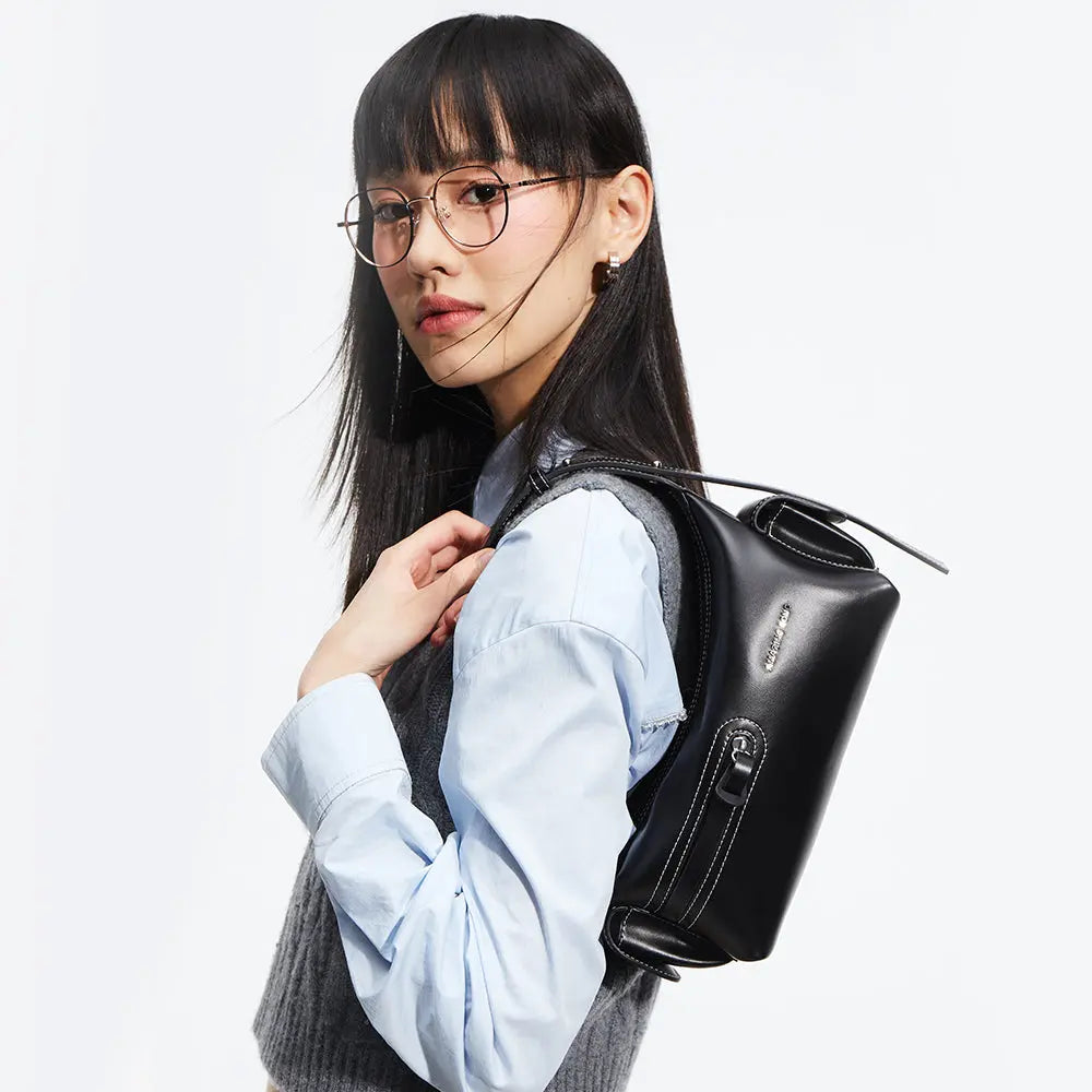 Stylish woman with glasses wearing a grey vest and blue shirt carrying a black handbag